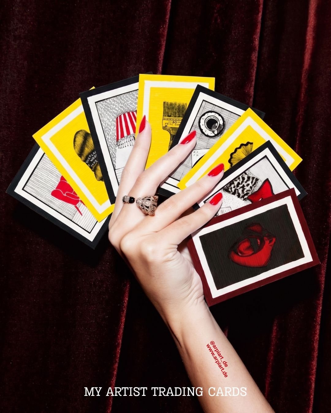 A hand fanning out artist trading cards in yellow, black and red